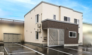 介護施設の建物外観。2階建てのベージュ色の新築建物と駐車場
